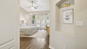 Une chambre à coucher comprenant un lit, un ventilateur de plafond, une fenêtre et une porte donnant sur une autre pièce.