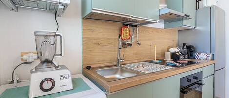 A compact kitchen with a Bosch blender, a microwave, a sink with a wooden countertop, and a refrigerator.