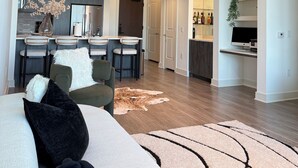 Een moderne woonkamer met een bank, een salontafel en een vloerkleed. Er is een keukenhoek met een eettafel en stoelen.