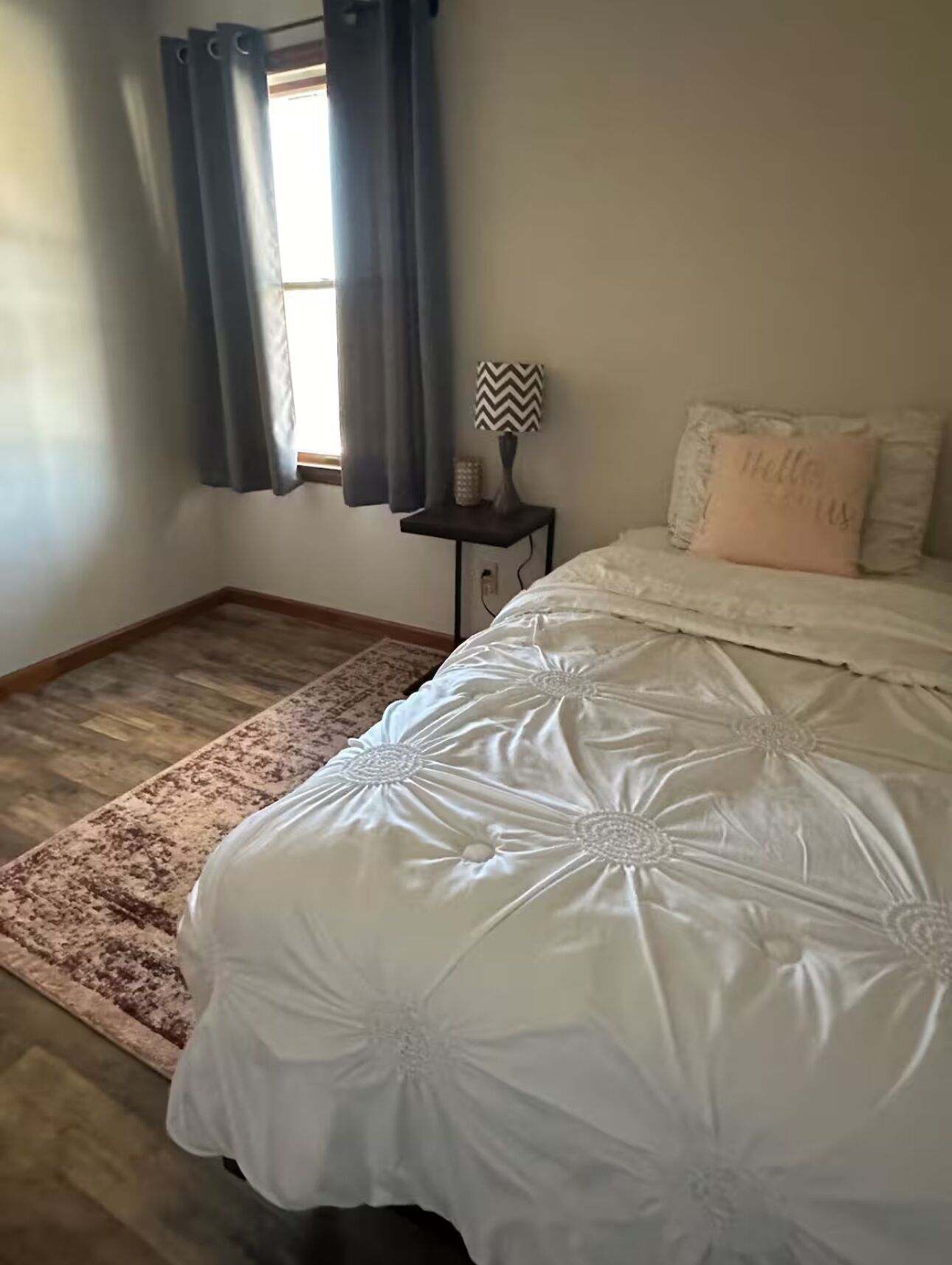 A bedroom with a large bed, a nightstand, a lamp, and a window with curtains.