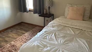 A bedroom with a large bed, a nightstand, a lamp, and a window with curtains.