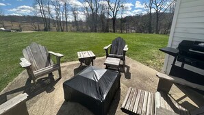 Um pátio externo com cadeiras Adirondack, uma mesa coberta e uma churrasqueira.