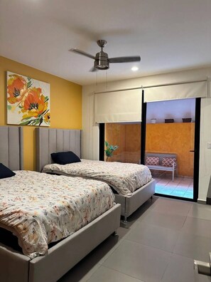 Ein Schlafzimmer mit zwei Betten, einem Deckenventilator, einem Gemälde und einer Glastür, die auf einen Balkon führt.