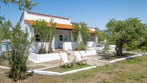 A white building with a red-tiled roof, a small porch, and two wooden chairs in the front yard. - Odyssey Eco Farm Glamping (Troizinia)