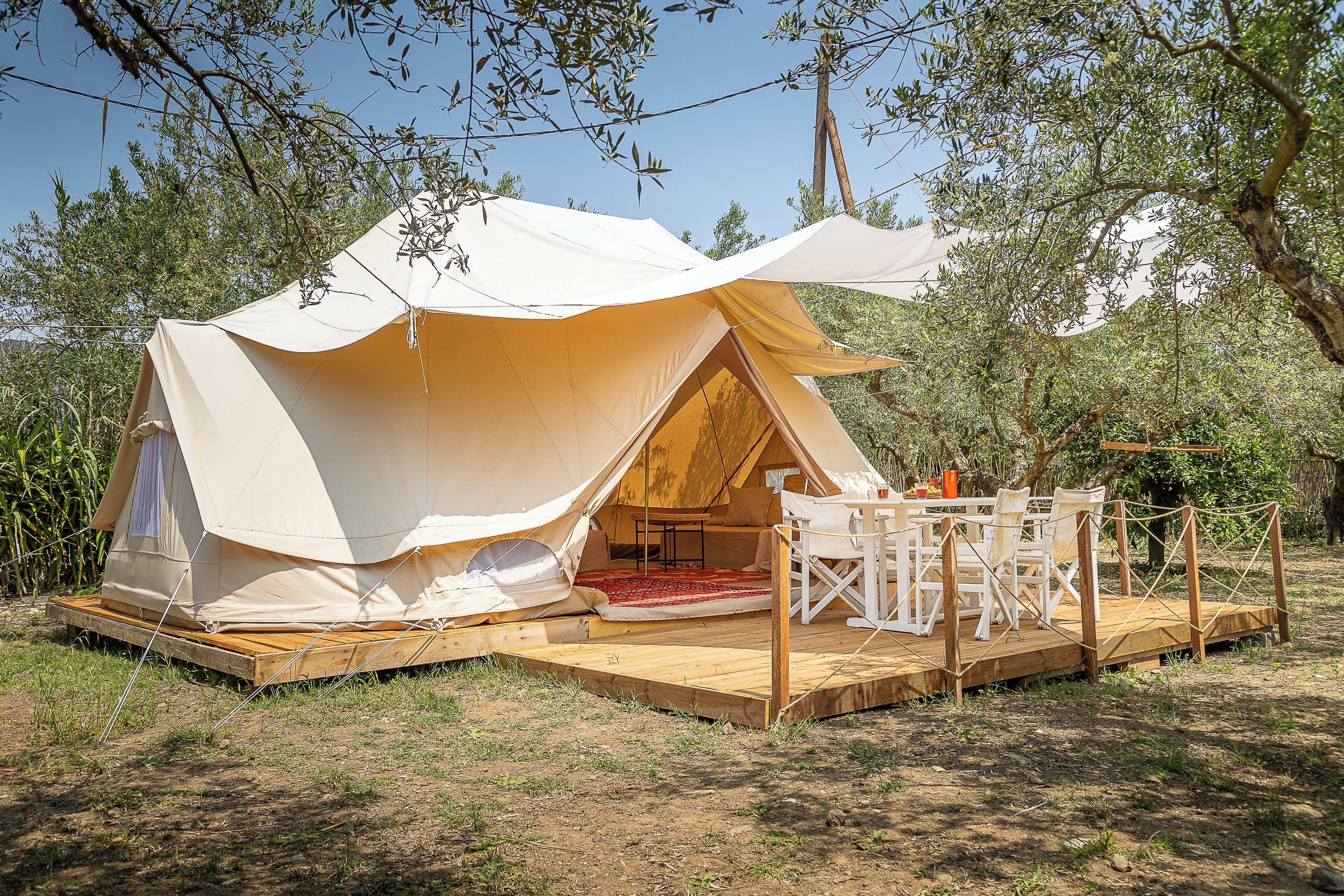 A large tent with a wooden deck and seating area, surrounded by trees.