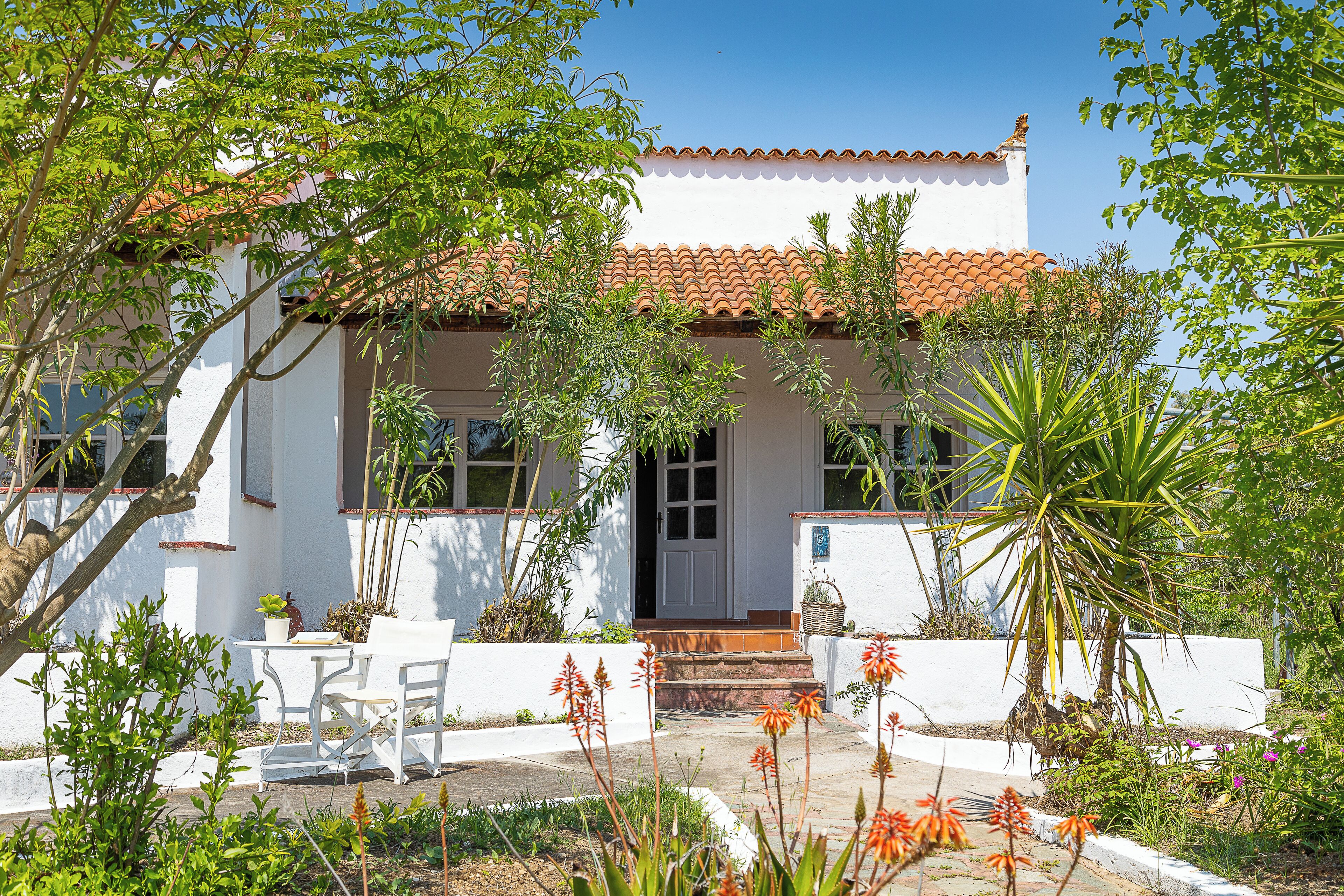 A white building with a tiled roof, surrounded by greenery and a small patio area.
