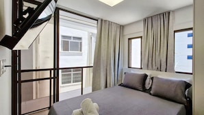 Une chambre d’hôtel comprenant un lit, deux oreillers, une fenêtre avec des rideaux, un balcon avec une balustrade et un escalier.