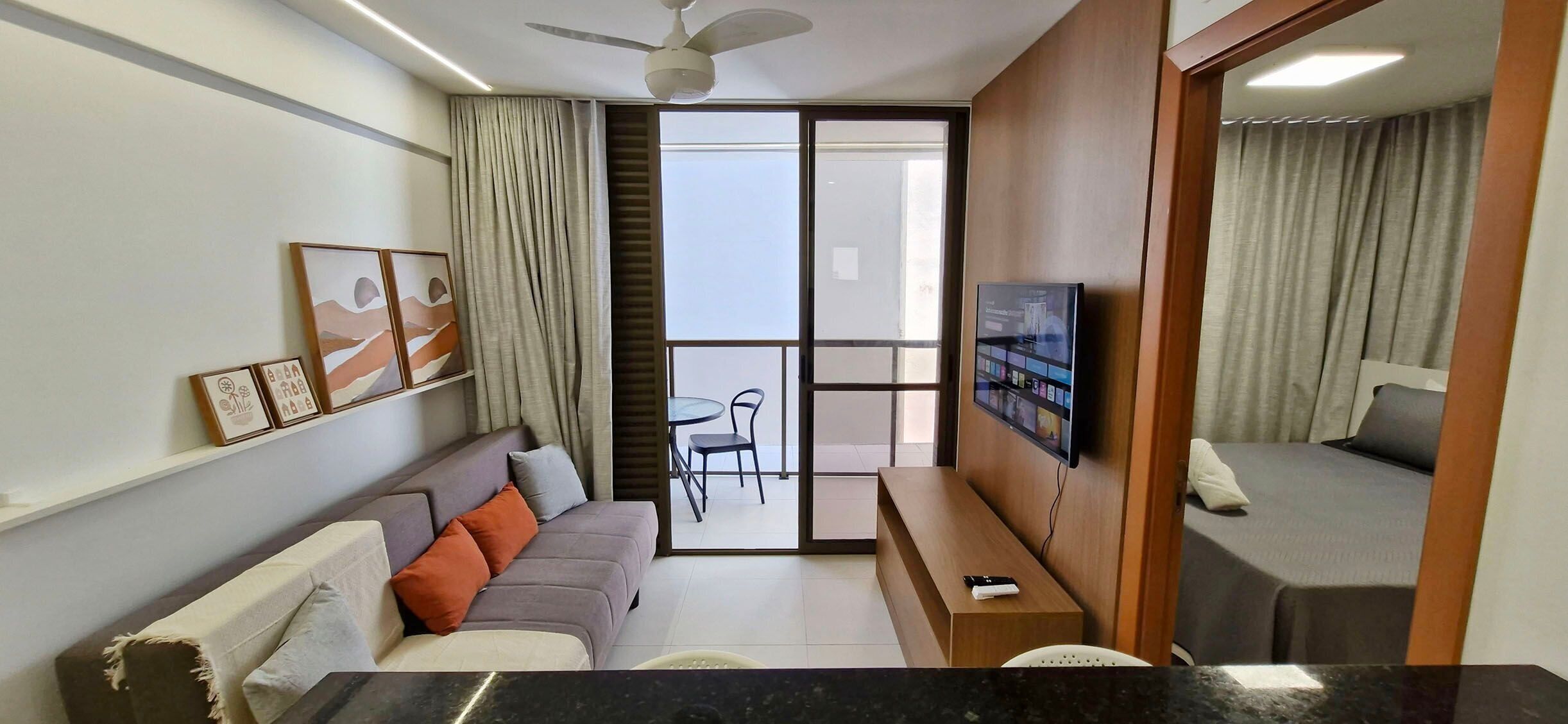 Een moderne woonkamer met een bank, een salontafel, een televisie en een balkon met een tafel en stoelen.