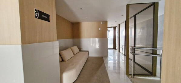 A modern hotel corridor with a sofa, a sign reading "TERREO", and a glass door leading to a balcony. - COGRA0104 - Graça Prime Residence (Salvador)