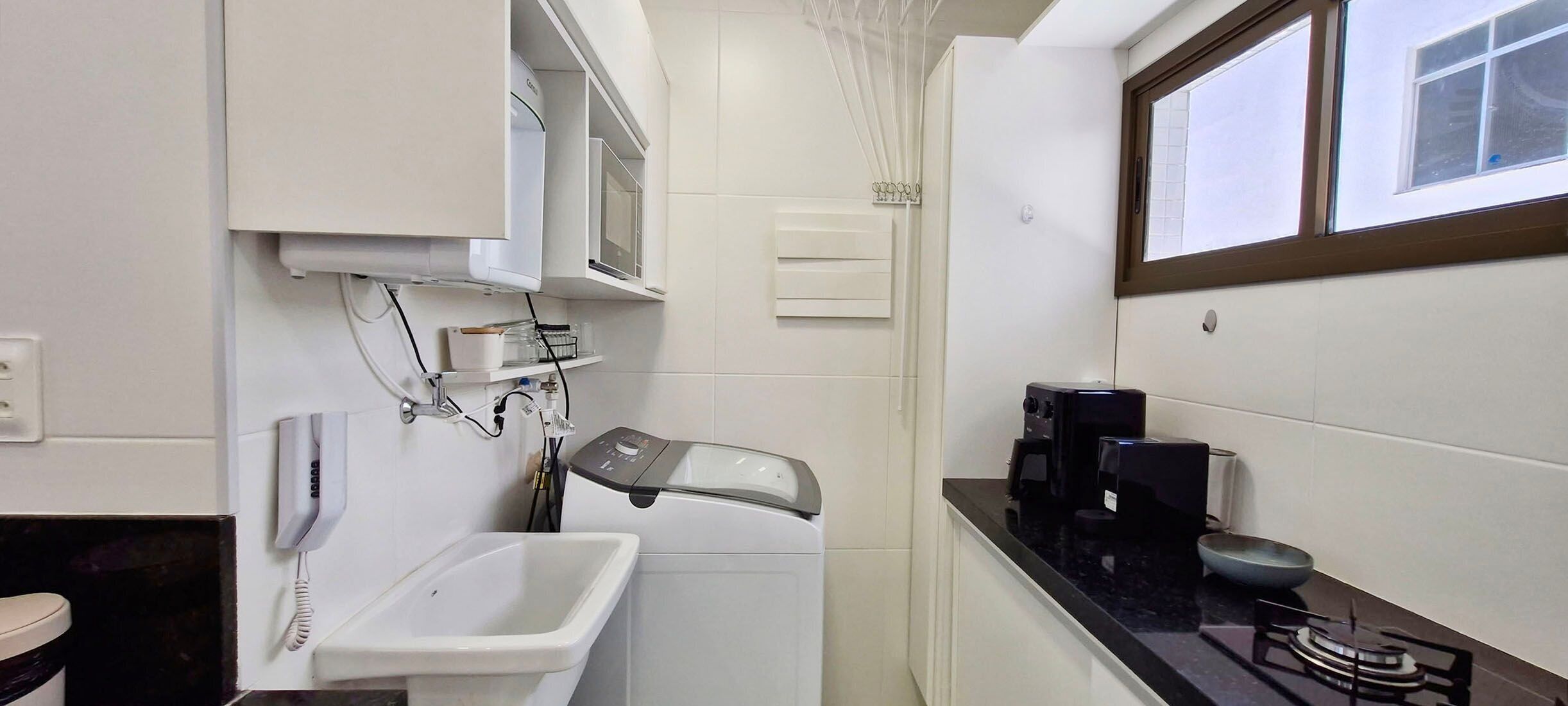 A compact bathroom with a sink, a mirror, a towel rack, a heater, a coffee maker, and a window.