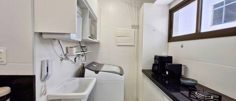 A compact bathroom with a sink, a mirror, a towel rack, a heater, a coffee maker, and a window.