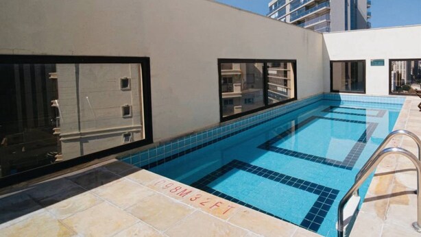 A rooftop swimming pool with clear blue water, surrounded by a beige wall and large windows. - FARIA LIMA HOTEL COM VARANDA GARDEN  (São Paulo)