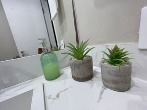A bathroom with a white sink, a green glass bottle, and three potted plants. - FARIA LIMA HOTEL COM VARANDA GARDEN  (São Paulo)