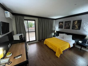 A hotel room with a bed, a desk, a chair, a telephone, a lamp, a TV, and a window with curtains. - FARIA LIMA HOTEL COM VARANDA GARDEN  (São Paulo)