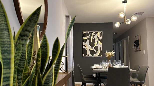 Ein moderner Essbereich mit Holzboden, einem runden Tisch und Stühlen. An der Wand hängt ein großer Spiegel und eine Deckenleuchte.