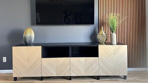 Ein modernes Wohnzimmer mit einem großen Flachbildfernseher an der Wand, einer Unterhaltungseinrichtung mit Holzvertäfelung im Fischgrätmuster darunter und einer Wand aus vertikalen Holzleisten zur Rechten.