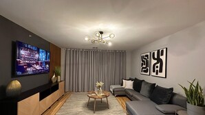 Ein modernes Wohnzimmer mit Flachbildfernseher, einer Couch, einem Couchtisch und einer Zimmerpflanze.