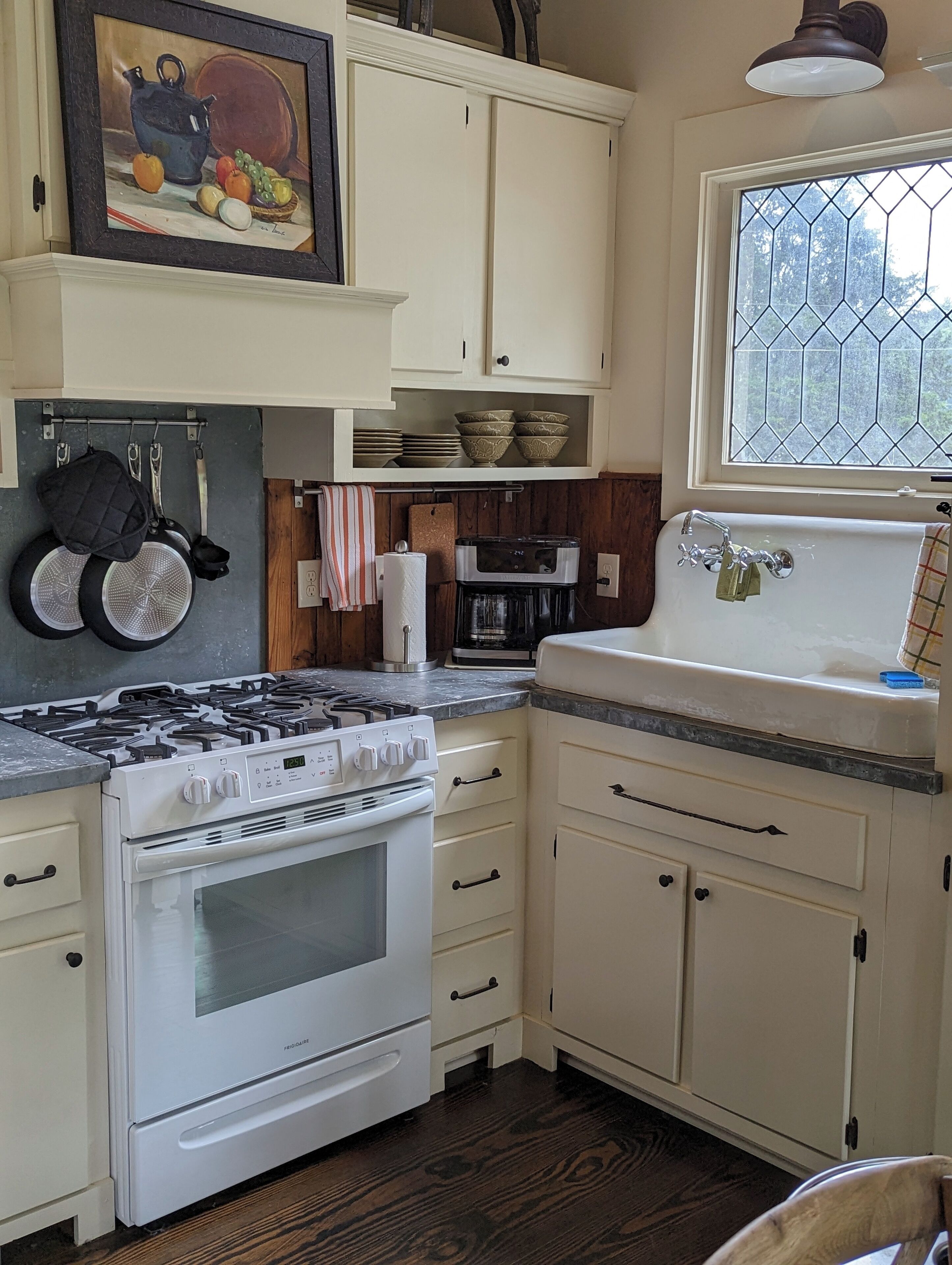 Una cocina con armarios blancos, estufa, pileta y ventana con diseño geométrico.
