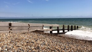 Ein Kiesstrand mit einem hölzernen Steg, der sich ins Meer erstreckt.