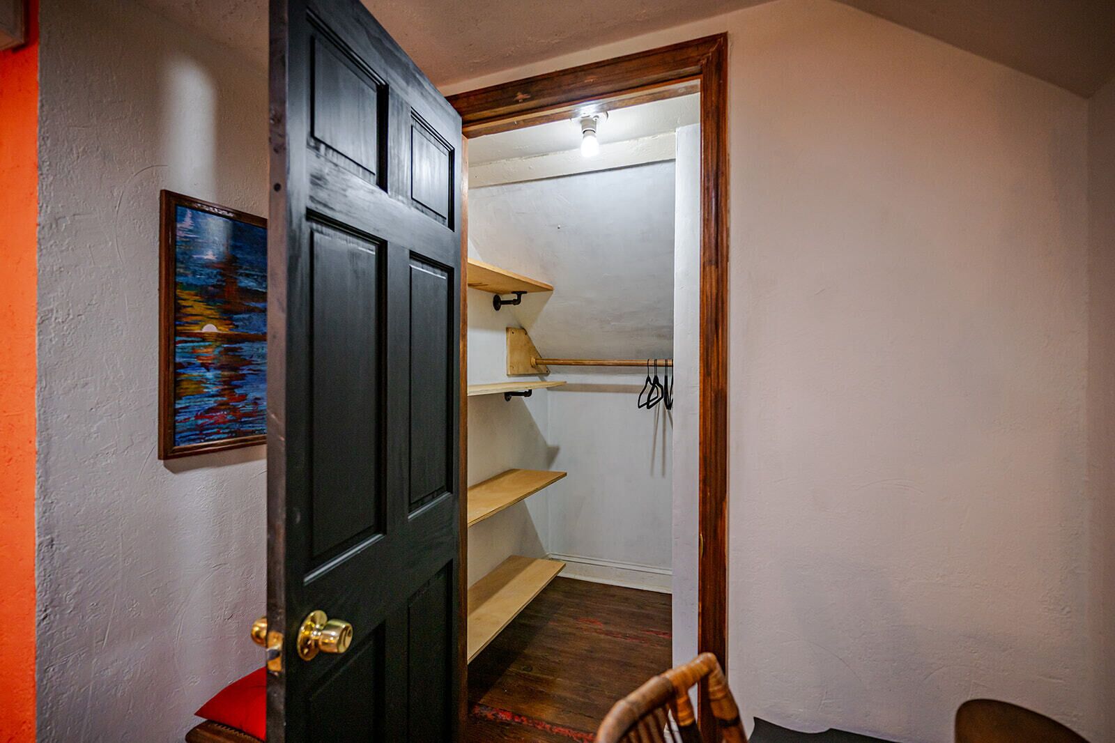 A hallway with a black door, a wooden chair, and a shelf with hanging items.
