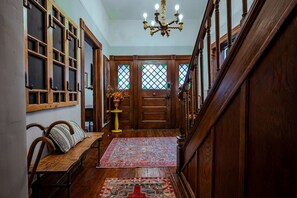A wooden staircase leading to a room with a chandelier, a wooden bench, and a patterned rug. - Grant Park 4BR Victorian Retreat Walk to Zoo & BeltLine - Private Parking Deck (Atlanta)
