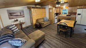 A cozy cabin interior with a wooden ceiling, a living area with a sofa and a dining table, and a kitchen with wooden cabinets and a refrigerator. - Amazing Waterfalls & Swim Hole at Dale Hollow Lake (albany)