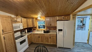 A kitchen with wooden cabinets, a white refrigerator, a stove, and a microwave. There is a window with a 'Welcome' sign above it. - Amazing Waterfalls & Swim Hole at Dale Hollow Lake (albany)