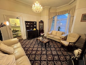 A living room with a patterned carpet, a chandelier, a sofa, a chair, a coffee table, and a window with blinds. - seaview guest house (Southport)