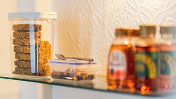 A glass jar with a spoon on a shelf, next to a patterned wall.