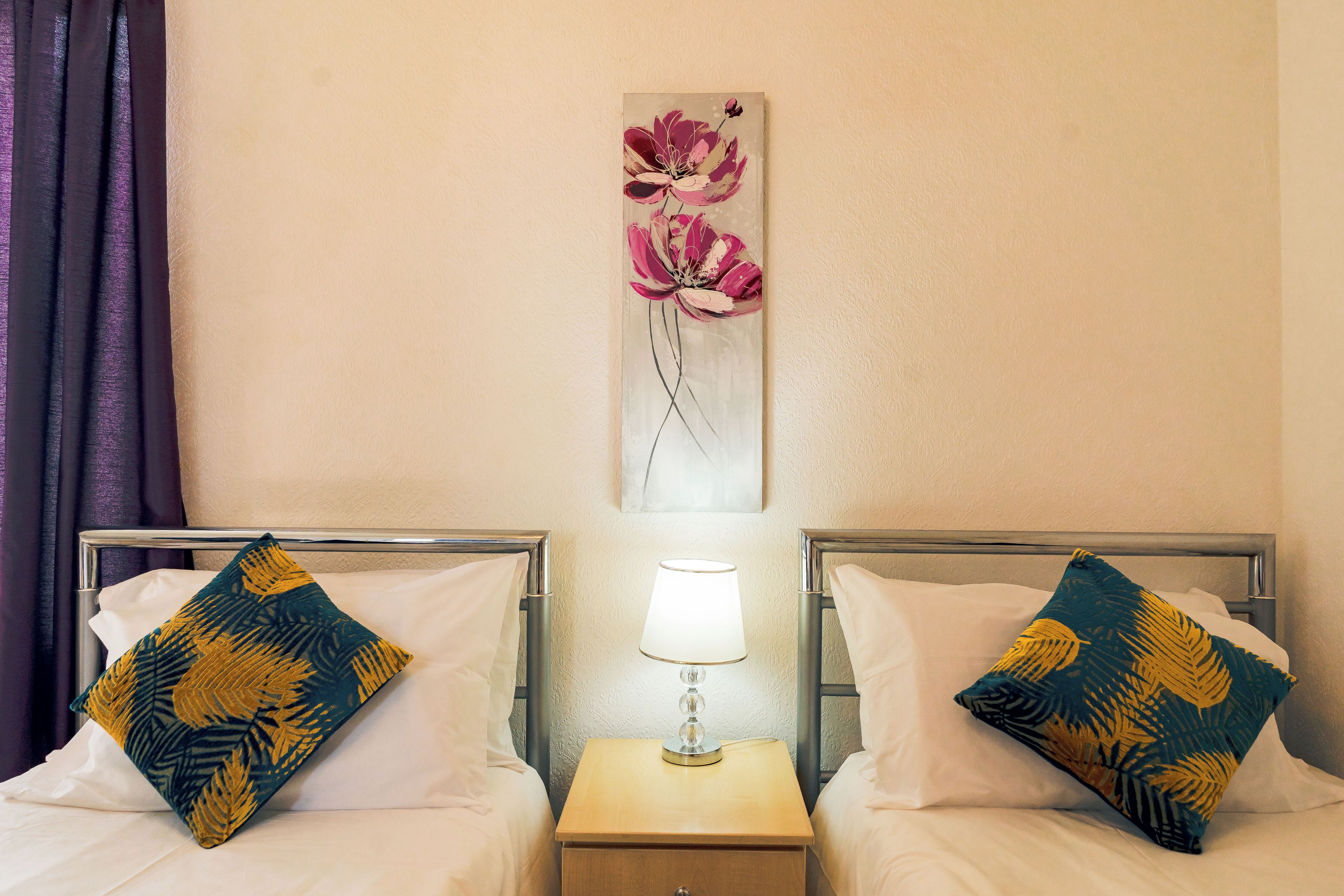 Habitación de hotel con dos camas, una mesita de noche con lámpara y una obra de arte floral en la pared.