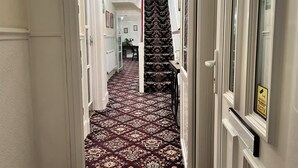 Un couloir avec un tapis à motifs, des murs blancs et un escalier recouvert d’un tapis à motifs.