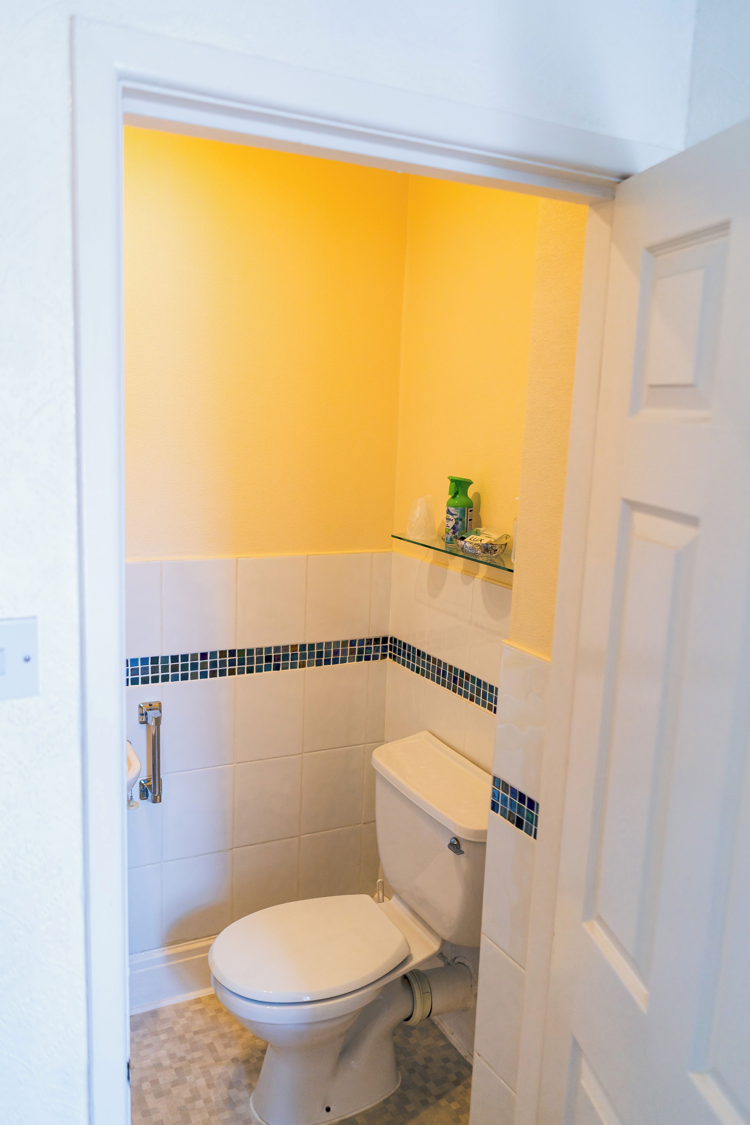 A small bathroom with a toilet, a glass shelf, and a tiled wall.