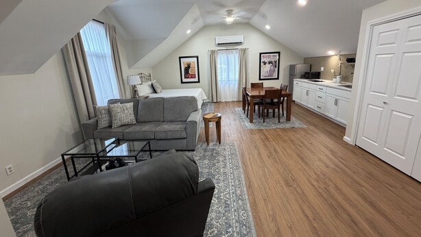 Un moderno apartamento tipo loft con cama en altura, zona de comedor, cocina y espacio de estar con sofá y mesa de centro.