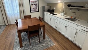 Una cocina compacta con armarios blancos, una mesa de comedor con sillas y un refrigerador pequeño.