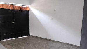 Una habitación con piso de baldosas, una puerta negra y un techo blanco con vigas a la vista.