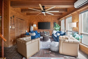 A wooden interior with a ceiling fan, a flat-screen TV, two sofas, a coffee table, and large windows. - Little Creek Retreat close to Boone & Blowing Rock (Boone)