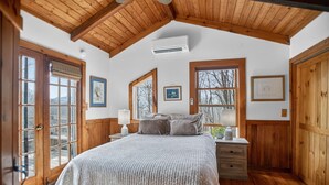 Een slaapkamer met een houten plafond, een bed, een nachtkastje en een raam met uitzicht.