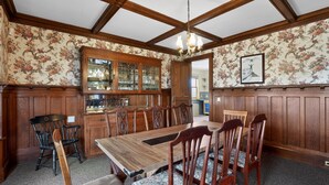 Un comedor con una mesa y sillas de madera, una lámpara de araña y papel tapiz floral.