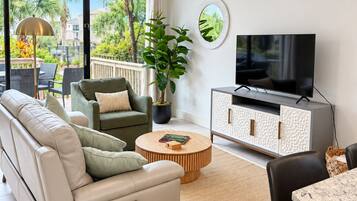 Un soggiorno moderno con divano, poltrona, tavolino, televisore e un balcone con piante.