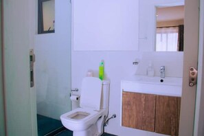 A bathroom with a toilet, a sink, and a mirror. - Mivida by Garden city Mall (Nairobi)