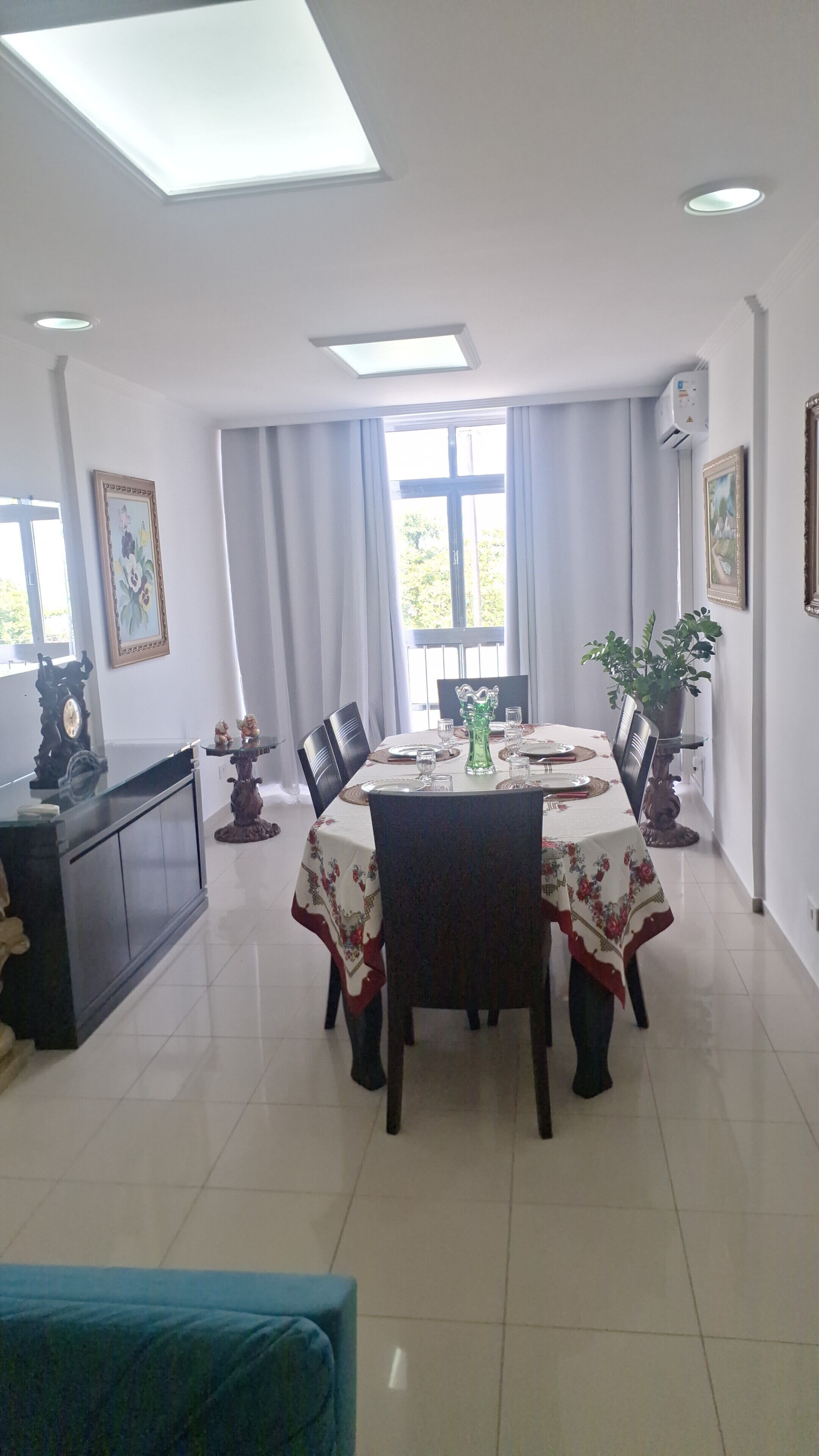 Un coin repas avec une table dressée pour six personnes, entourée de chaises, d’un buffet et d’une plante en pot.