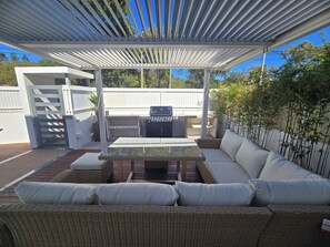 A covered patio with a grill, wicker furniture, and a white fence. - Casa Cliff by Sesimbra Sun Sea (Maça - Sesimbra)