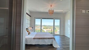 A bedroom with a large bed, a view of the city, and a modern chandelier. - Casa Cliff by Sesimbra Sun Sea (Maça - Sesimbra)