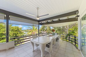 A balcony with a white table and chairs, a ceiling fan, and a view of palm trees and a house. - Beautiful Oceanview Home with private pool, In walking distance from Mambo Beach (Willemstad)