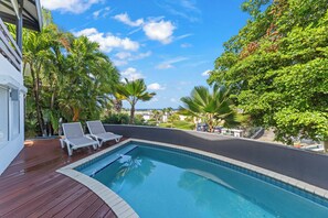 A swimming pool with lounge chairs, surrounded by lush greenery and a clear blue sky. - Beautiful Oceanview Home with private pool, In walking distance from Mambo Beach (Willemstad)