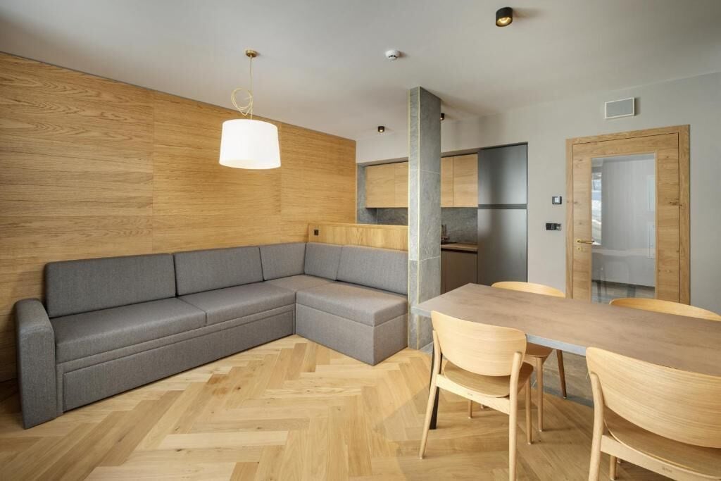 Eine moderne Küche mit einer Wand in Holzoptik, einem grauen Ecksofa und einem Holzesstisch mit Stühlen.