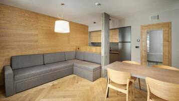 Eine moderne Küche mit einer Wand in Holzoptik, einem grauen Ecksofa und einem Holzesstisch mit Stühlen.