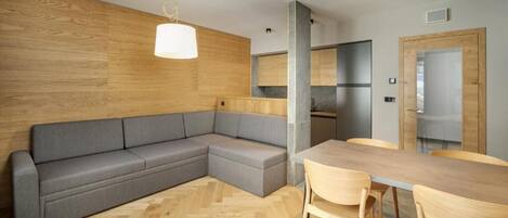 A modern kitchen with a wooden accent wall, a grey sectional sofa, and a wooden dining table with chairs.