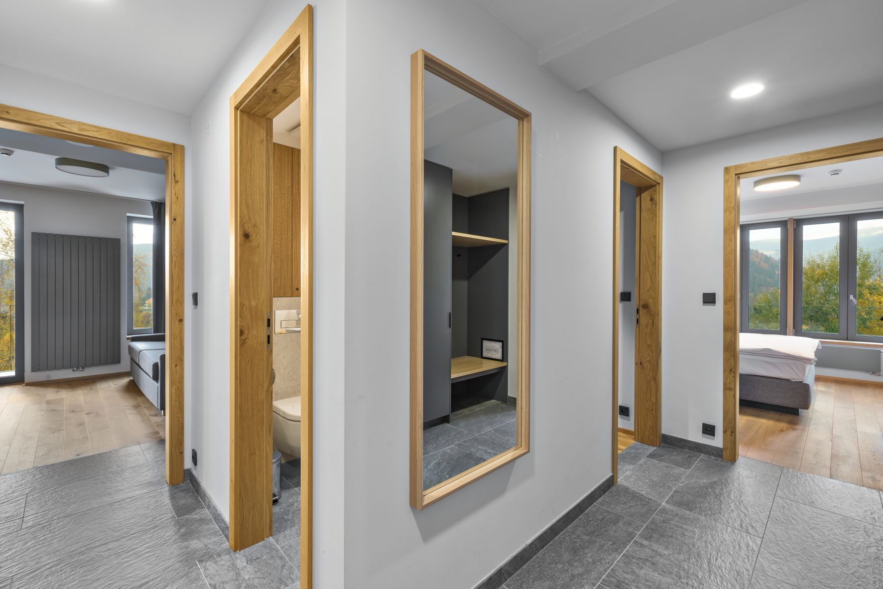 Un interior moderno con un pasillo central, puertas de madera y vistas a un dormitorio con cama y ventana.