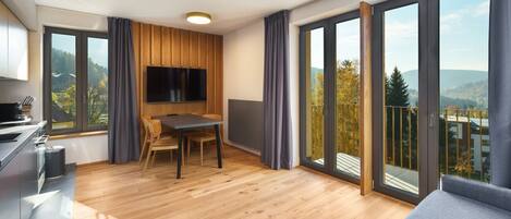 Un apartamento moderno con comedor, televisor montado en un panel de madera y grandes puertas corredizas de vidrio que dan a un balcón con vistas panorámicas.